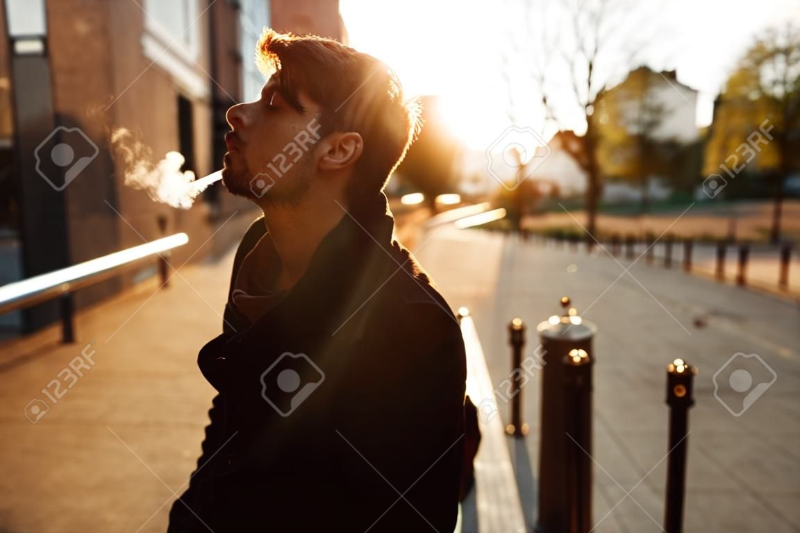 Young man smokes at sunset in the middle of the city