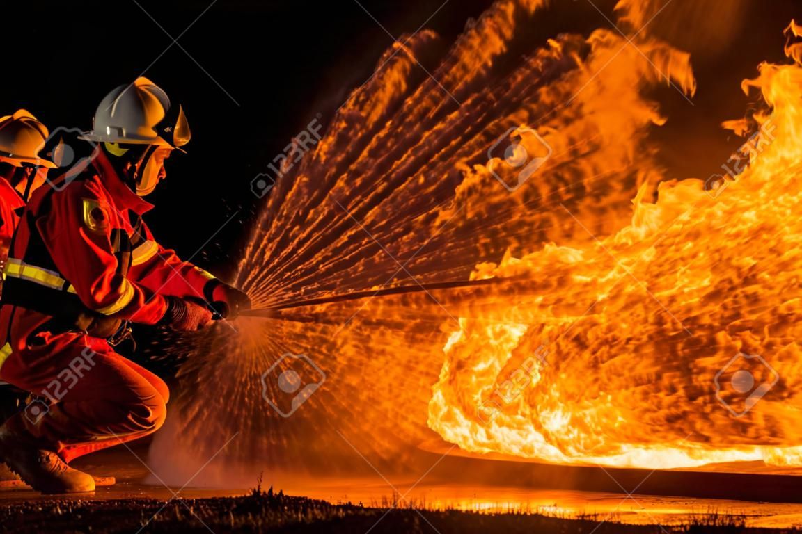 Feuerwehrleute, die einen Feuerlöscher vom Typ Wirbelwassernebel verwenden, um mit der Feuerflamme aus Öl zu kämpfen, um das Feuer zu kontrollieren und sich nicht auszubreiten. Feuerwehr- und Arbeitsschutzkonzept.