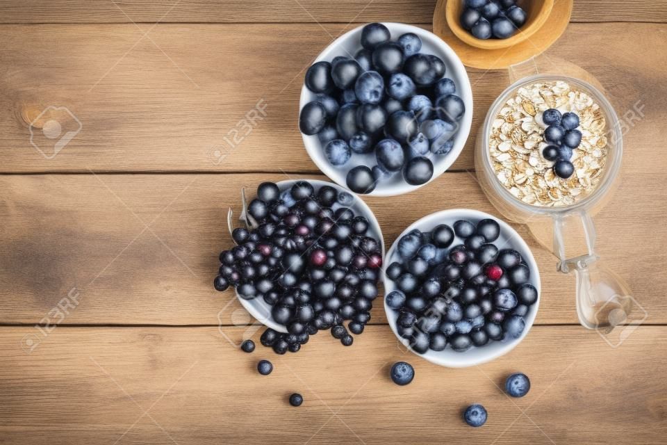 Desayuno del verano. Ingredientes para el desayuno saludable - bayas, fruta y muesli en la mesa de madera blanca, primer plano vista superior horizontal. Tiro macro enfoque selectivo