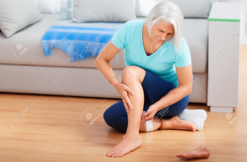 Frau mittleren Alters, die zu Hause unter Schmerzen im Bein leidet, Nahaufnahme. Konzept der körperlichen Verletzung.