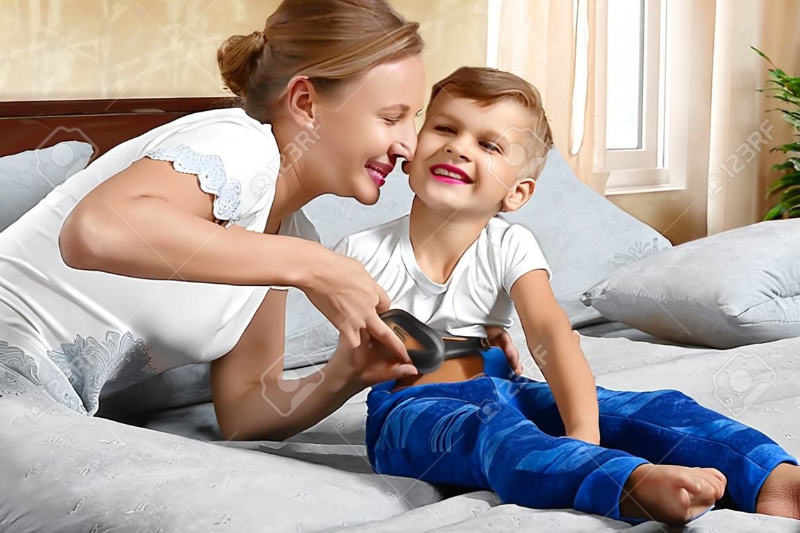 Mother tickling son. The parent teases the child. Fun games with mom. Mother and son on bed