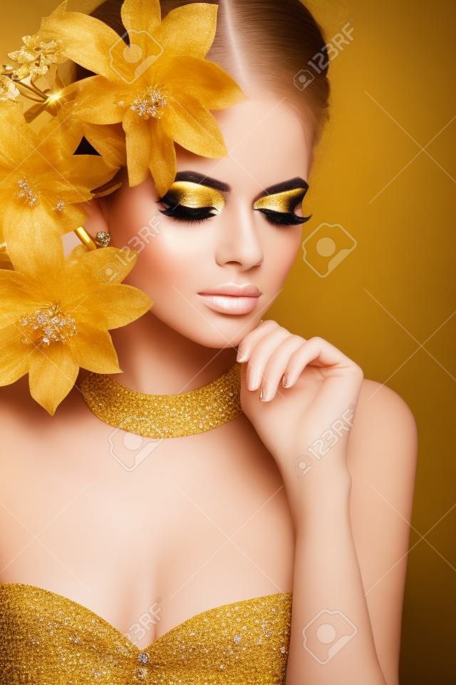 Makijaż Glamour. Dziewczyna zbliżenie twarzy. Uroda portret kobiety ze złotymi kwiatami. Biżuteria złota. Fryzura. Luksusowa zdjęcia