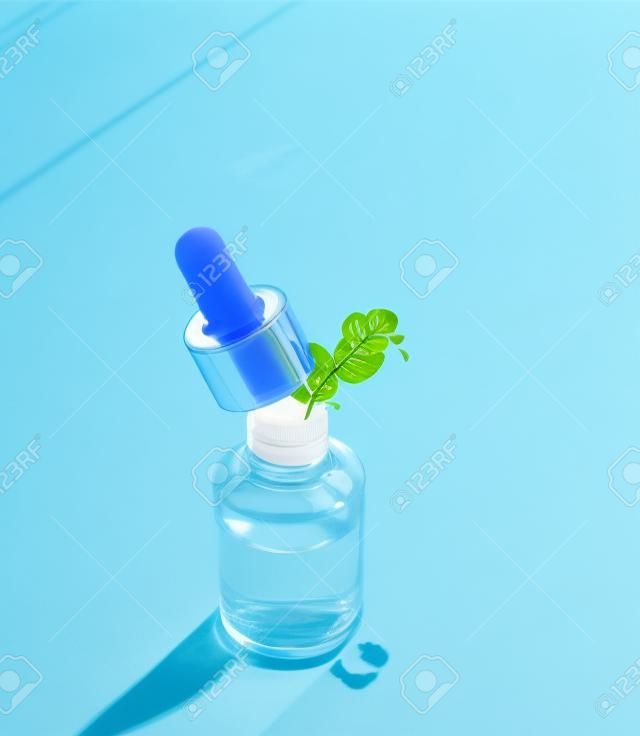 Transparent cosmetic bottle with pipette standing on blue background with palm leaves shadow. Facial skin care concept. Natural vegan cosmetic. Serum or skin essential oil. Modern beauty trend