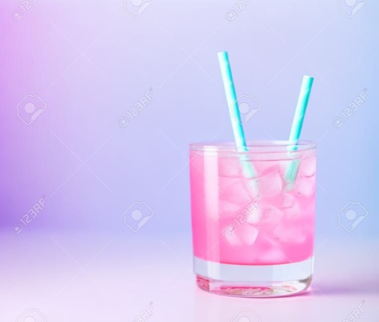 Bevanda rinfrescante ghiacciata rosa in vetro con cannuccia di carta su sfondo blu. Copia spazio. Cocktail estivo rosa pastello.