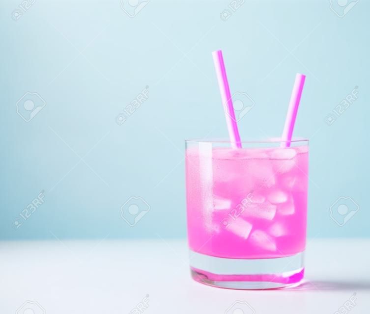 青い背景に紙の飲み物ストローとガラスのピンクのアイスリフレッシュメントドリンク。スペースをコピーします。夏のパステルピンクのカクテル。