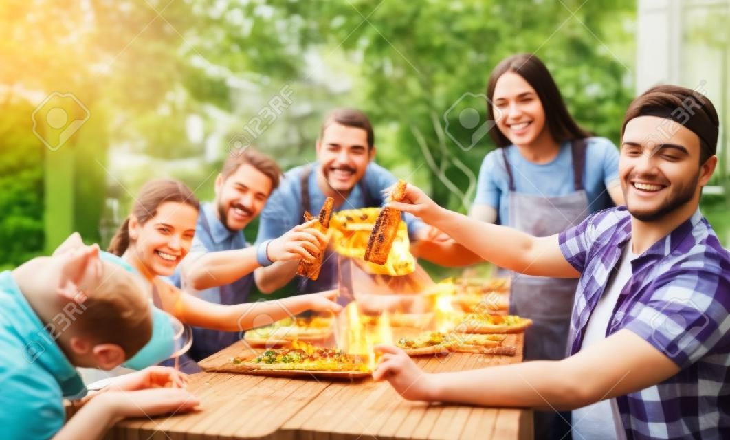幸福觀與年輕人在家裡享受食物一起 - 快樂的朋友吃飯，敬酒，在花園裡燒烤組
