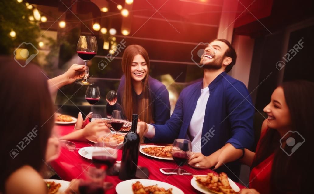 Jonge vrienden die plezier hebben met het drinken van rode wijn op het balkon op het huis diner party - Gelukkige mensen eten bbq eten in chique alternatieve restaurant samen - Eetgelegenheid lifestyle concept op gedesatureerd filter