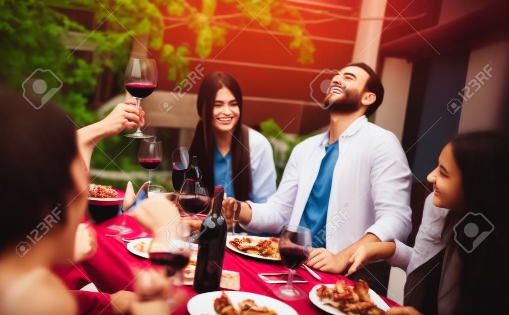 Jeunes amis s'amusant à boire du vin rouge sur le balcon lors d'un dîner à la maison - Des gens heureux qui mangent de la nourriture pour barbecue dans un restaurant alternatif chic ensemble - Concept de style de vie sur filtre désaturé