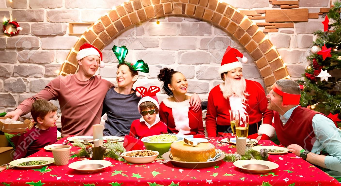 Group photo of multi generation family on santa hats clothes having fun at christmas fest house party - Winter holiday x mas concept with parents and children eating together - Warm cosy red filter