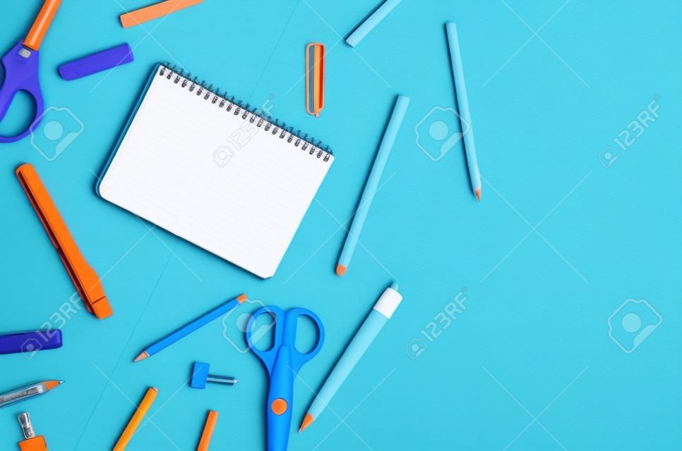 Notebook, blue and orange school supplies on blue background. Education concept. View from above with copy space. Mockup, flat lay