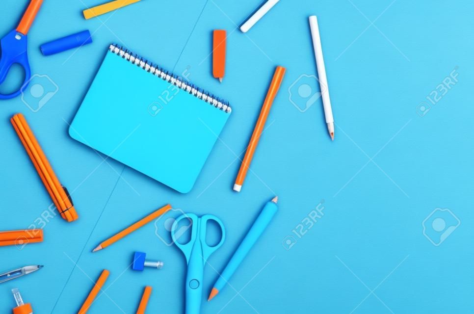 Notebook, blue and orange school supplies on blue background. Education concept. View from above with copy space. Mockup, flat lay