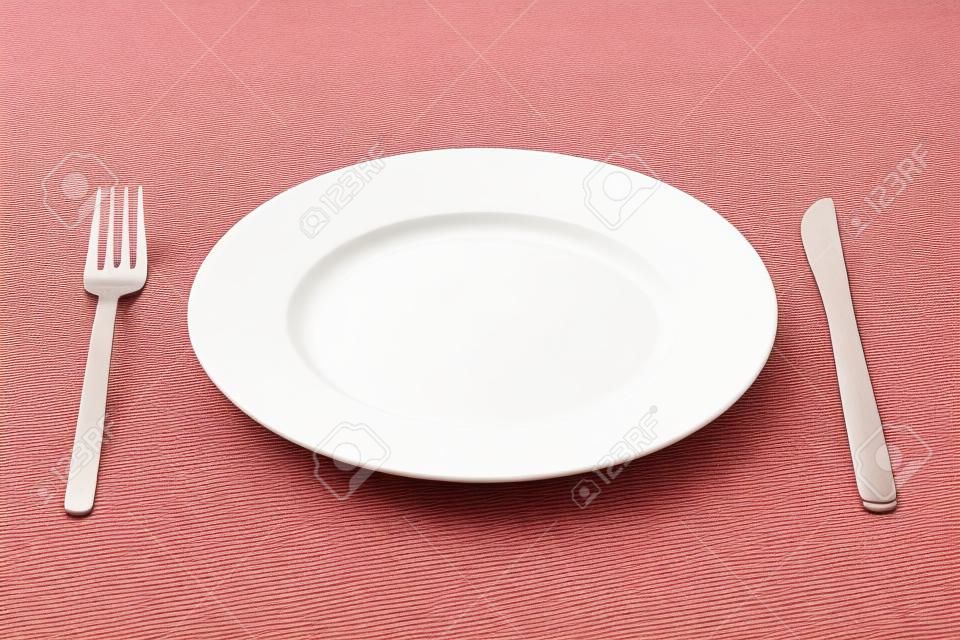 White empty plate with fork and knife on a red tablecloth 