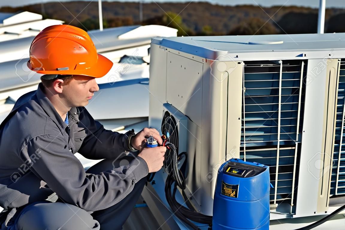 Klimaanlage Reparatur, junge Werker auf dem Dach Befestigungsklimaanlage Modell ist Elektriker tatsächlichen
