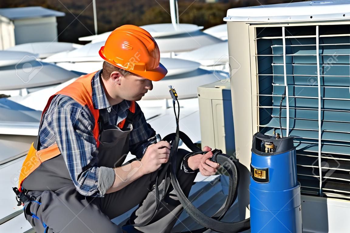 Klimaanlage Reparatur, junge Werker auf dem Dach Befestigungsklimaanlage Modell ist Elektriker tatsächlichen