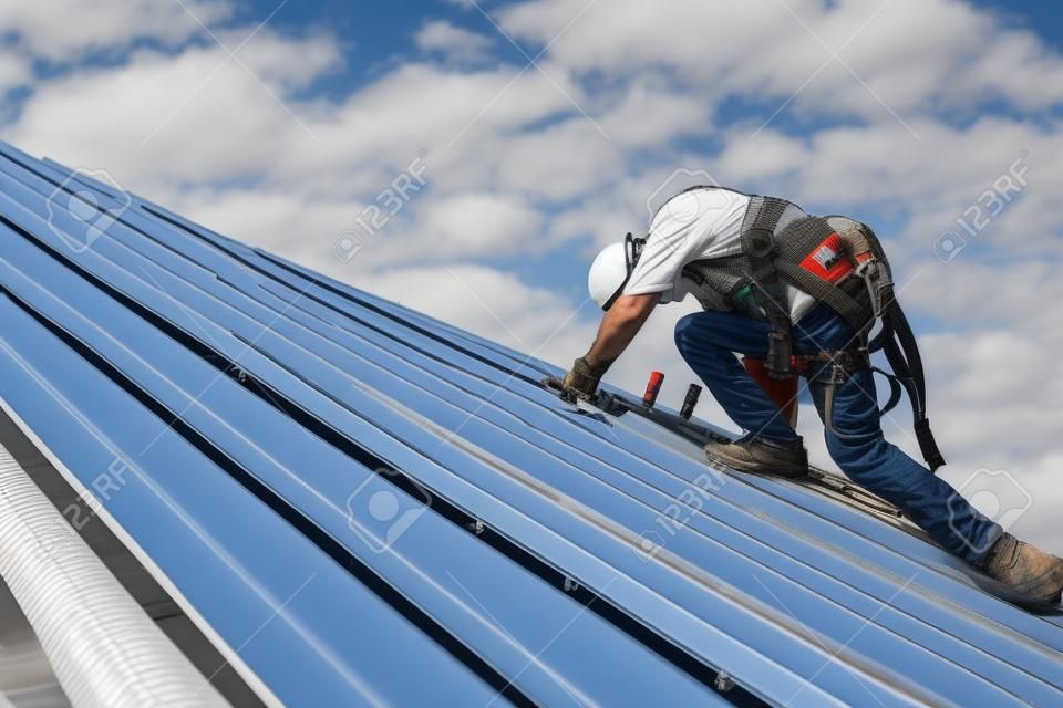 Dekarz pracujący na konstrukcji dachu budynku na placu budowy, dekarz za pomocą pneumatycznego lub pneumatycznego pistoletu do gwoździ i instalowanie blachy na nowym dachu.