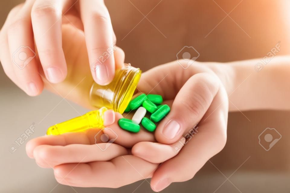Zbliżenie na ręce kobiety trzymającej pigułki witaminowe i wytrząsającej je z butelki na dłoni