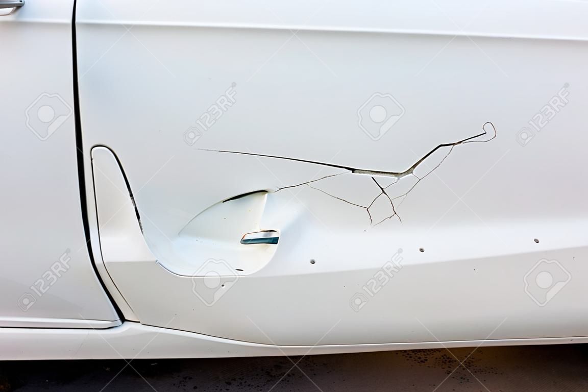 Wgniecenie na białym lakierze drzwi samochodu