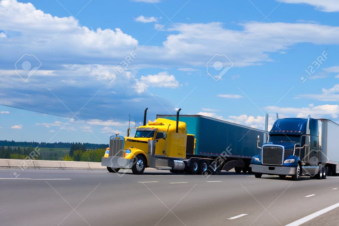 Two semi trucks of various models and manufacturers, a yellow classic American semi truck with a bulk trailer and a blue modern American semi truck with a high trailer for bulk cargo rushing along a wide highway next to each other