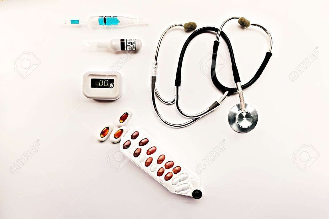 Stock photo of a stethoscope, a pulse oximeter, syringes and pills on a white background. There is nobody on the picture.