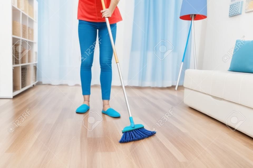Detail einer Frau, die Hausarbeit macht, einen Besen hält und den Boden fegt