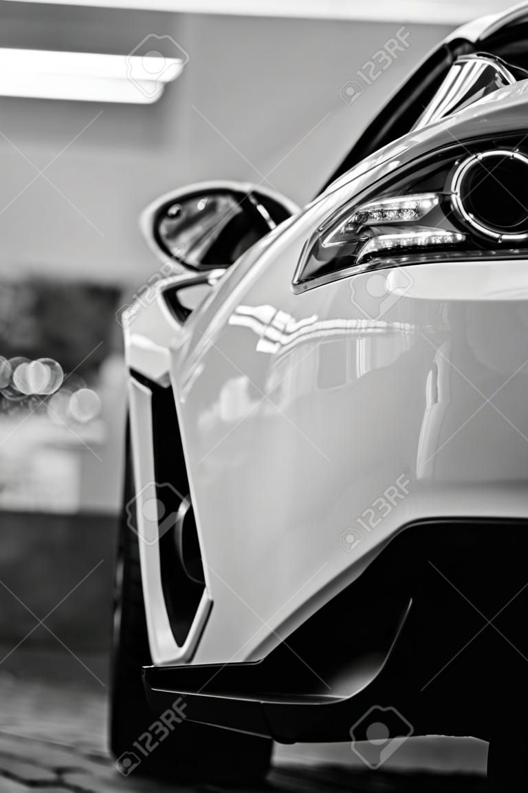 Bumper, Front of the white sports car.The car is on the road.Element for design.The headlight of the new clean white sports car has an aggressive shape with a piece of bonnet and black wheel, a bumper. black and white image