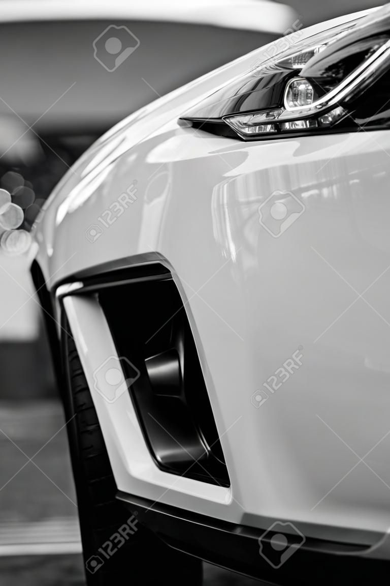 Bumper, Front of the white sports car.The car is on the road.Element for design.The headlight of the new clean white sports car has an aggressive shape with a piece of bonnet and black wheel, a bumper. black and white image