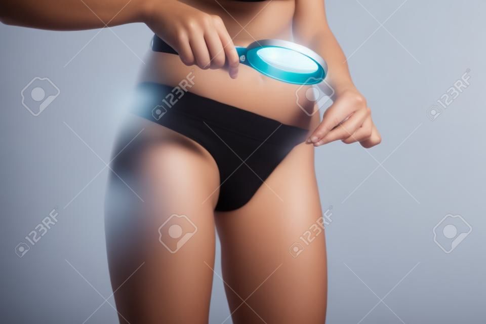 Unrecognizable woman examining genital area with magnifying glass on a white studio background.