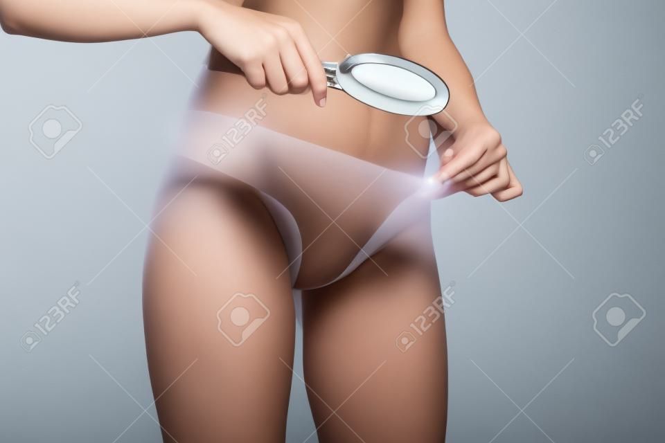 Mujer irreconocible examinando el área genital con lupa sobre un fondo de estudio blanco.