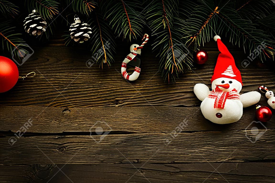 Kerstboom takken met kerstversieringen en sneeuwpop op houten textuur.