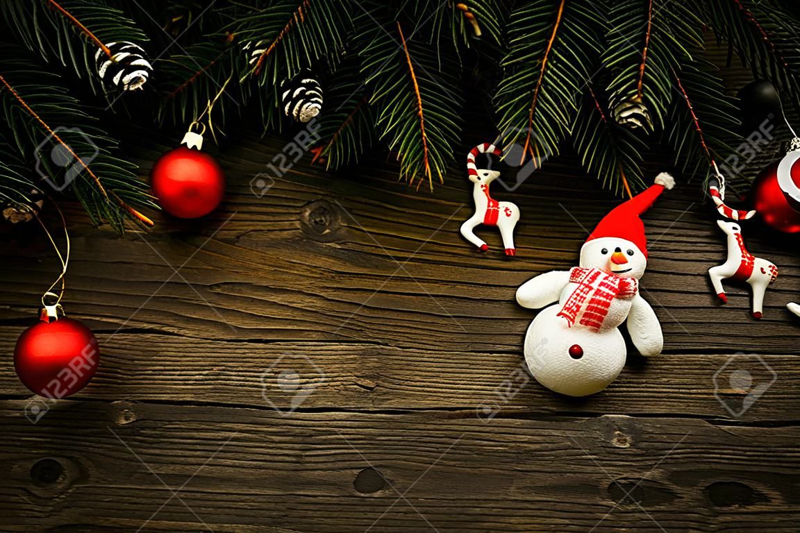 Christmas tree branches with christmas decorations and snowman on wooden texture.