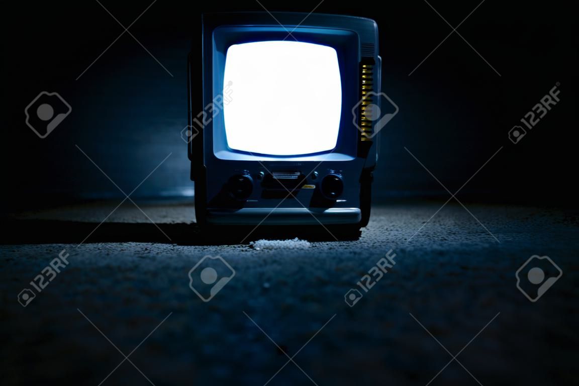 一个微型便携式电视屏幕，晚上在地板上有一个白色的屏幕发光。