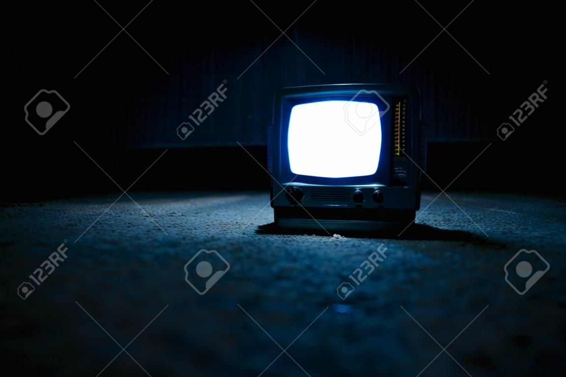 一个微型便携式电视屏幕，晚上在地板上有一个白色的屏幕发光。