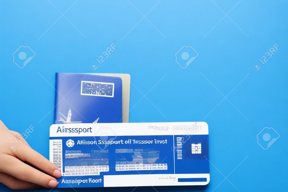 青い背景の上の女性の手でパスポートと航空券。旅行のコンセプト、コピースペース。