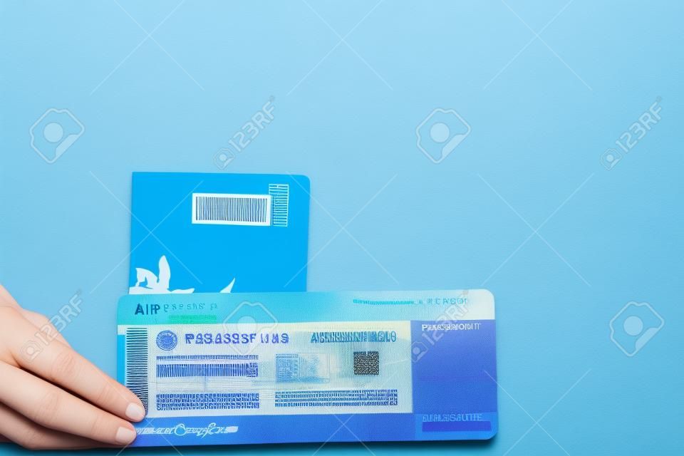 青い背景の上の女性の手でパスポートと航空券。旅行のコンセプト、コピースペース。