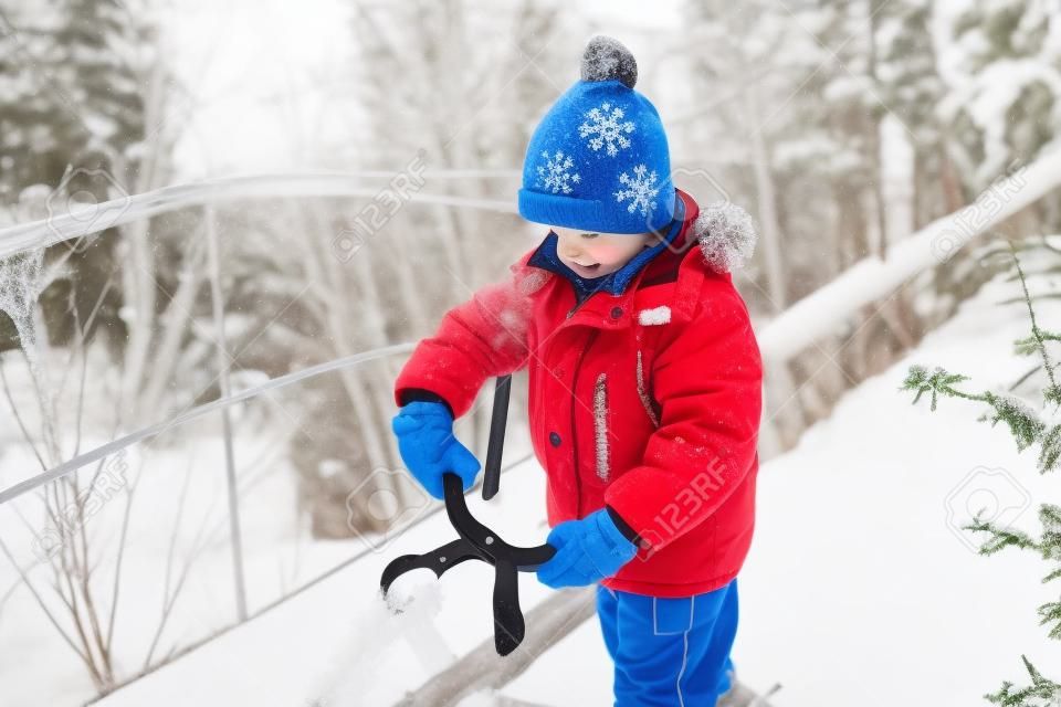Kleiner Junge macht Schneebälle mit Schneeballhersteller. Glückliches Kind, das mit Schnee spielt. Kaltes Winterwetter. Winteraktivitäten für Kinder