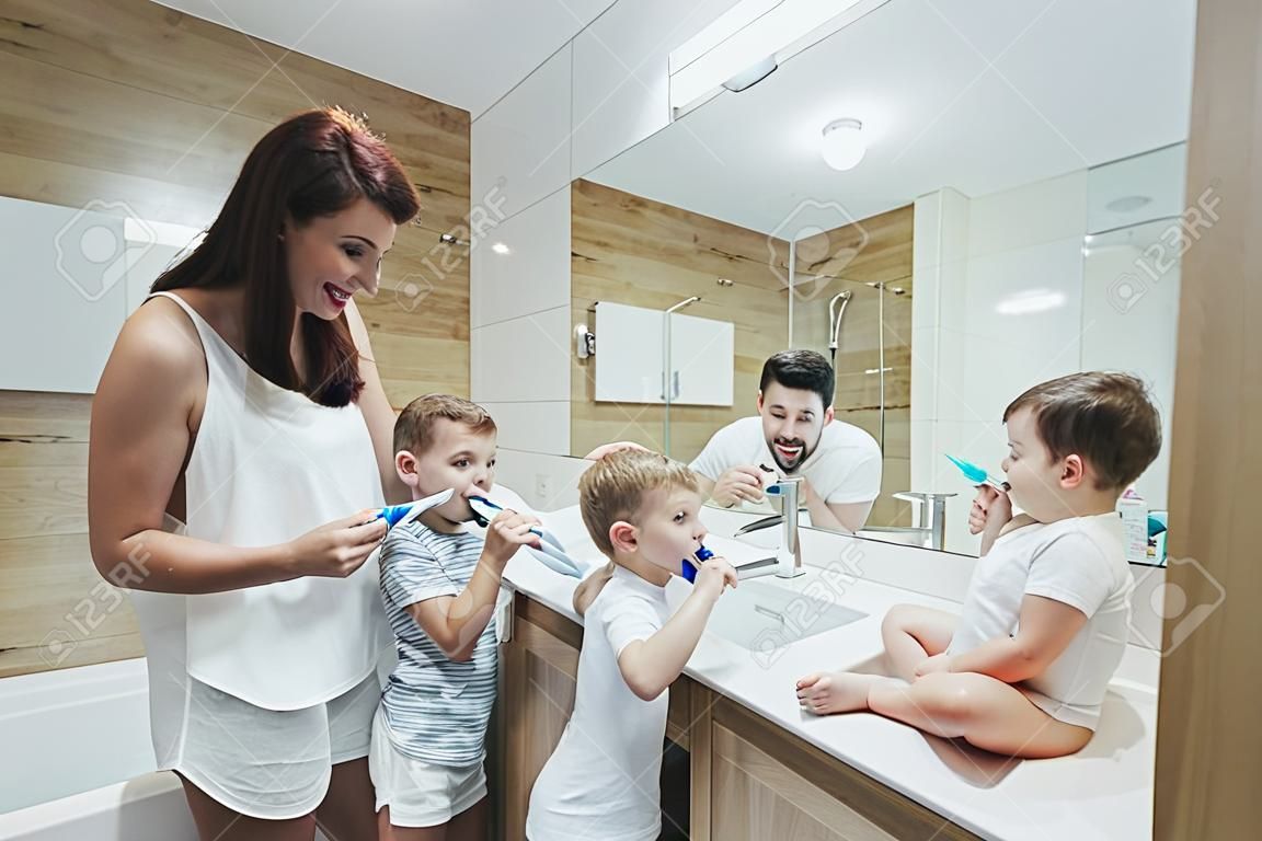 Młody szczęśliwy mężczyzna z rodziny, kobieta i dwoje małych dzieci, dwóch chłopców w plecaku myjących zęby razem w łazience