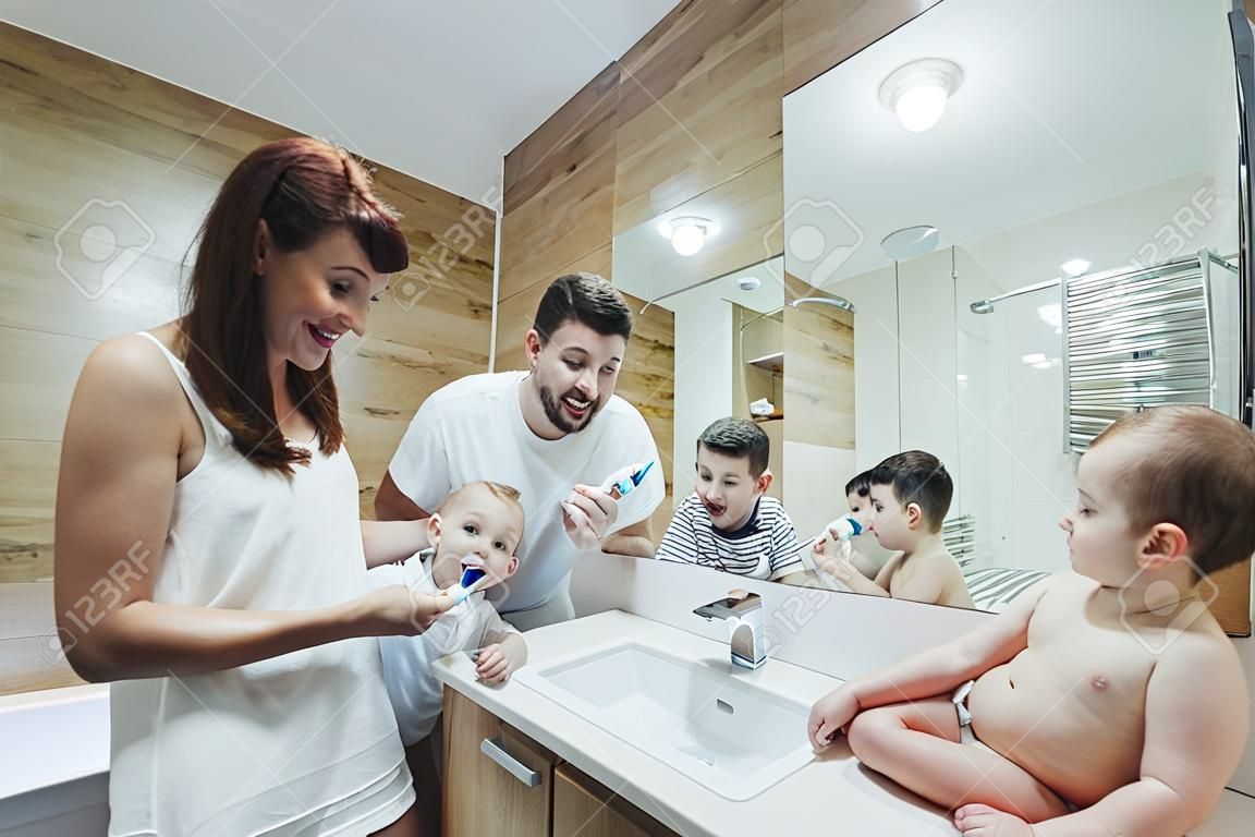 Młody szczęśliwy mężczyzna z rodziny, kobieta i dwoje małych dzieci, dwóch chłopców w plecaku myjących zęby razem w łazience