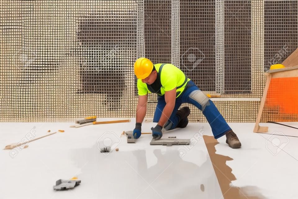 남성 건설 노동자가 대형 세라믹 타일을 설치합니다.