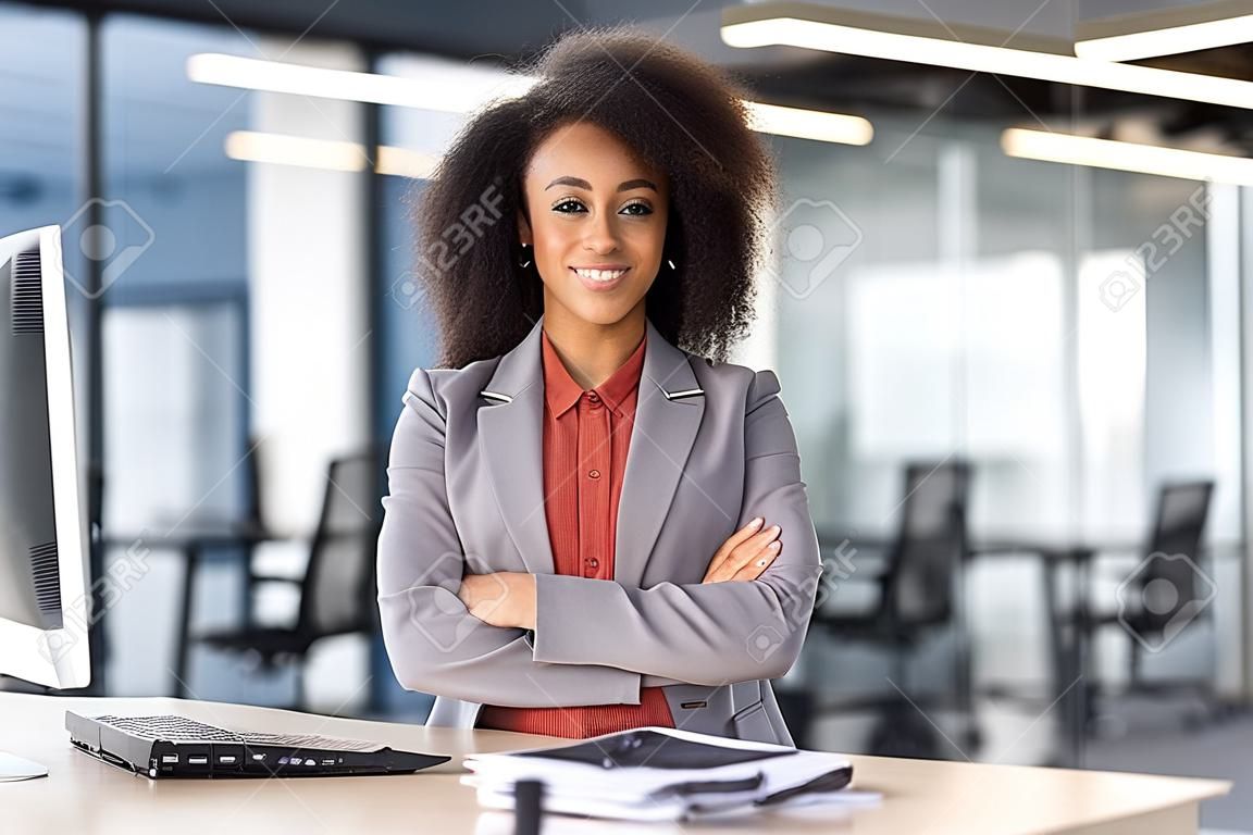 Professional African American businesswoman with curly hair standing confidently in a modern office setting.