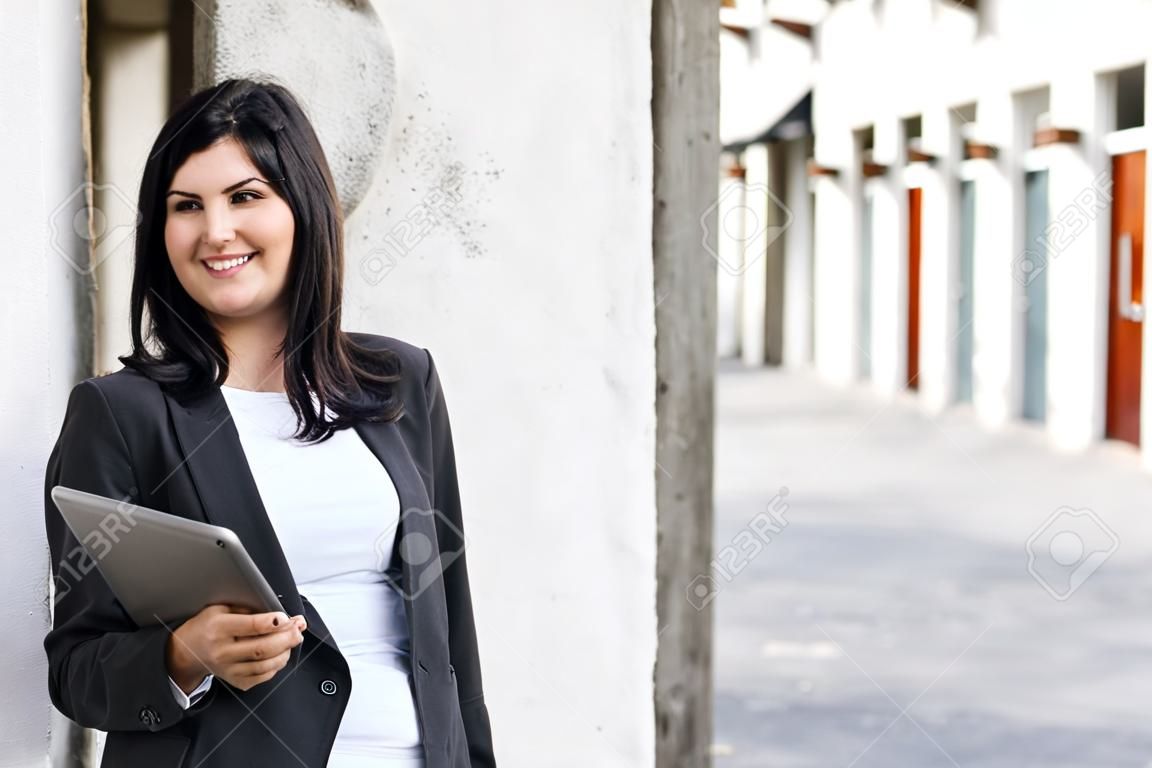 Smiling brunette smiling and holding a tablet in the street
