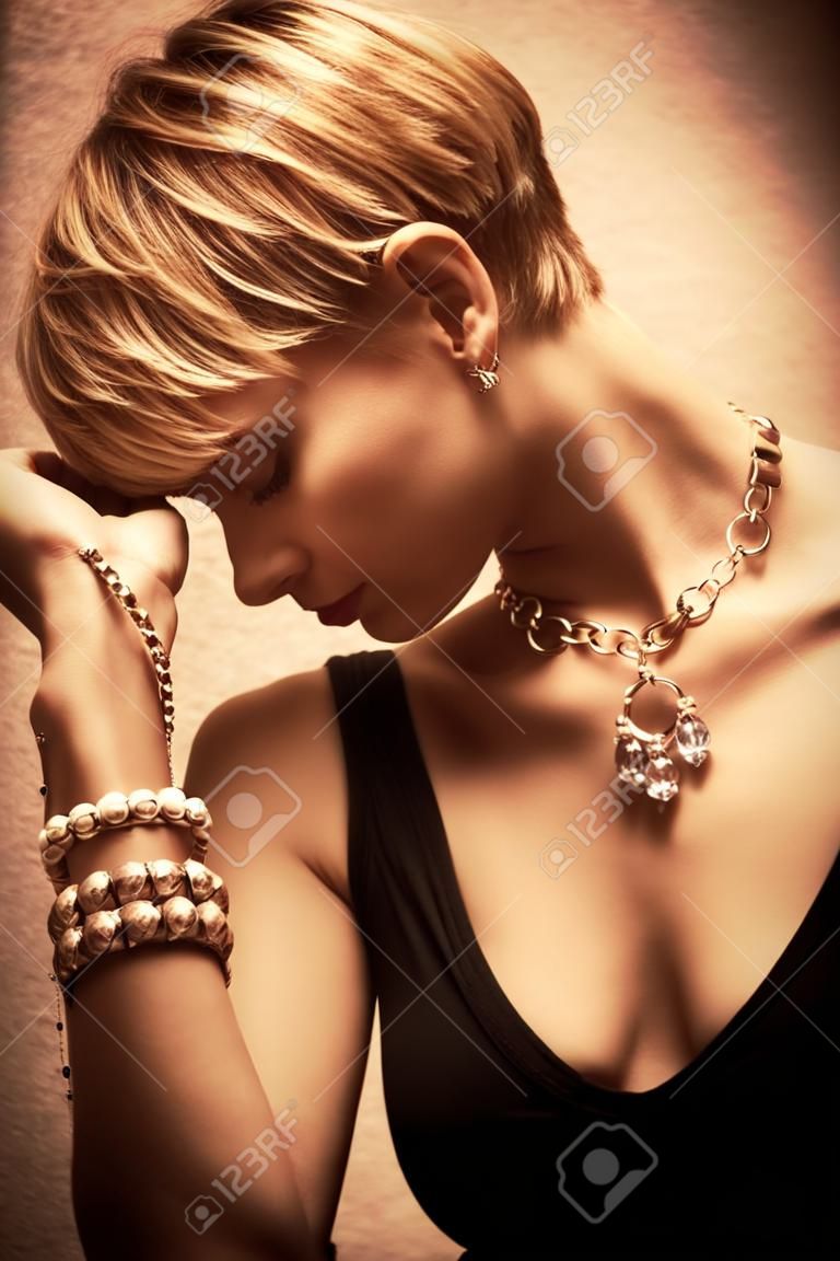 cabelo curto loiro elegante jovem mulher retrato vestindo jóias, colar e monte de pulseiras, tiro indoor, vista lateral