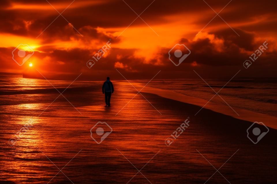Silhouette eines Mannes, der bei dramatischem Sonnenuntergang am Meeresstrand spazieren geht