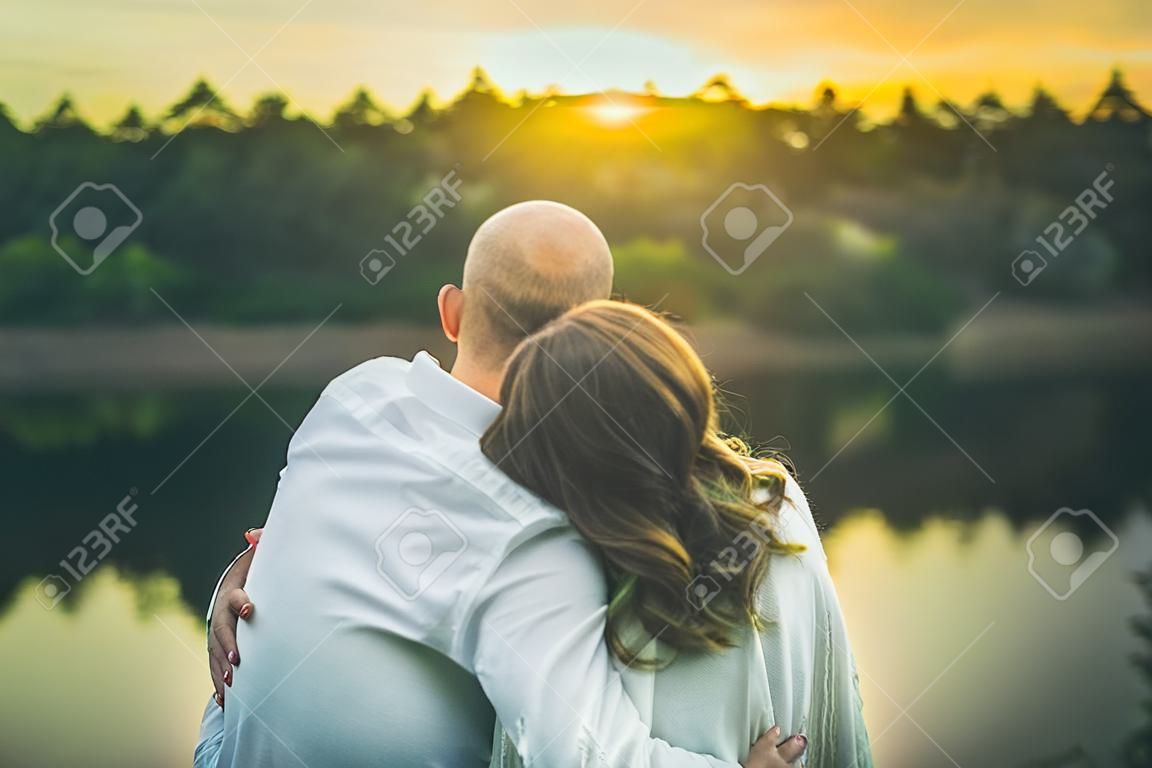 couple is hugging in white shirt and sweater looking to the yellow sunset sitting crop close