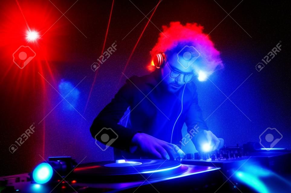 夜總會的DJ播放音樂在甲板上用黑膠唱片耳機光照明泡吧派對現場