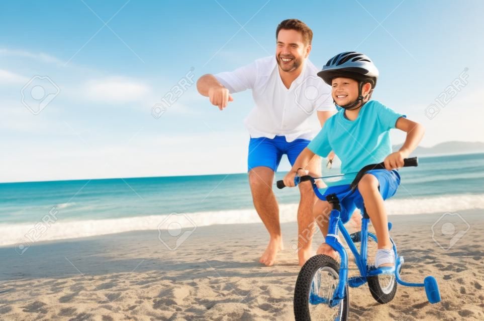 Vater und Sohn lernen, ein Fahrrad am Strand, die Spaß zusammen fahren
