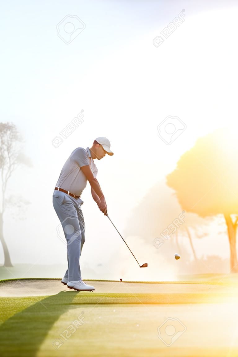 Golfer chipping op het groen bij zonsopgang op de golfbaan in mistige omstandigheden