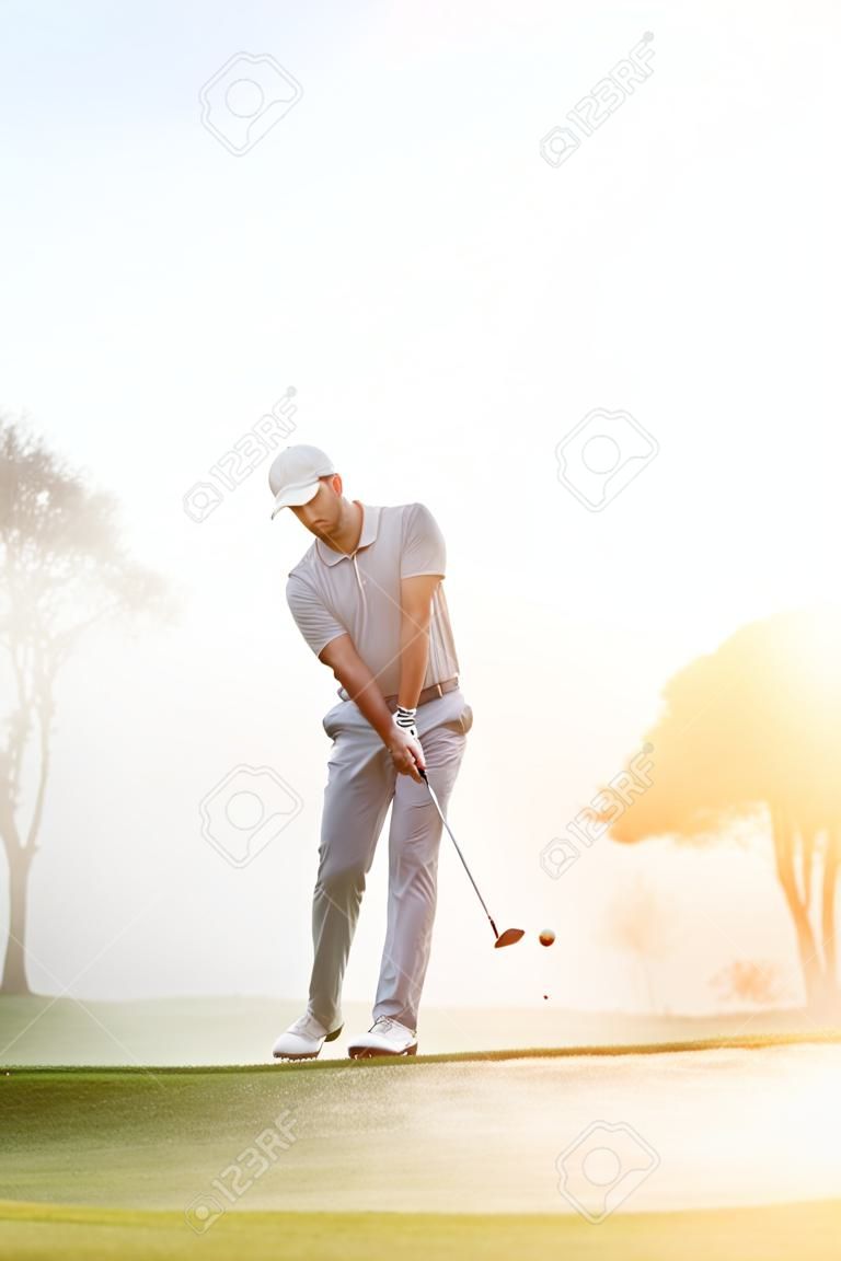 Golfista de astillado en el verde en la salida del sol sobre el campo de golf en condiciones brumosas