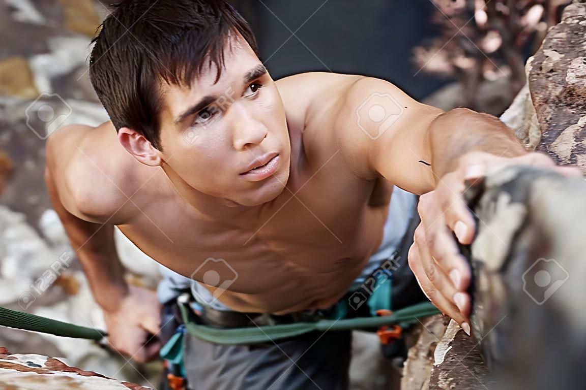 A good looking man with a face of concentration who is rock climbing