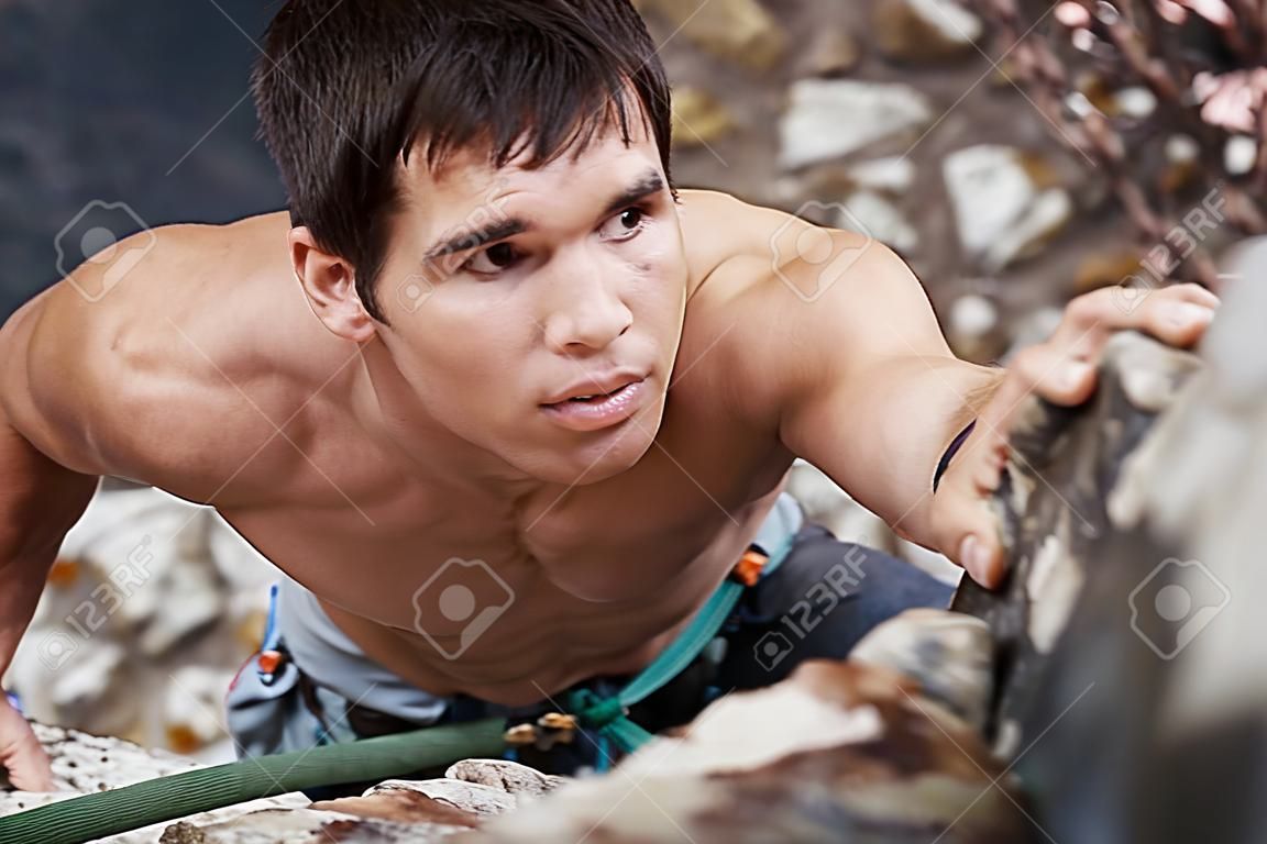 A good looking man with a face of concentration who is rock climbing