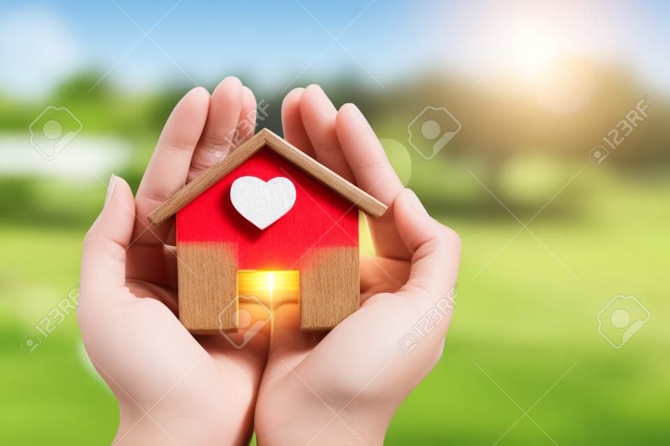 Vrouw hand met een huis model steek een rood hart in het zonlicht in het openbaar park, Leningen voor onroerend goed of bespaar geld om een nieuw huis voor familie te kopen in het toekomstige concept.